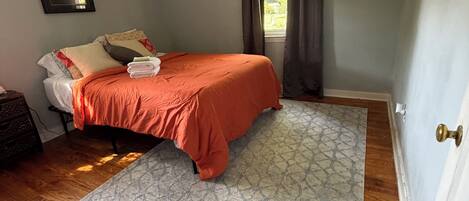 A bedroom with a bed, a ceiling fan, a window with curtains, and a patterned rug.