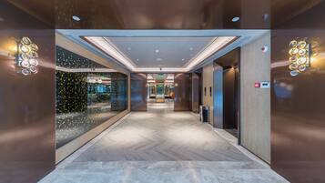 A modern elevator interior with a herringbone floor pattern, recessed lighting, and a glass wall with decorative lights.