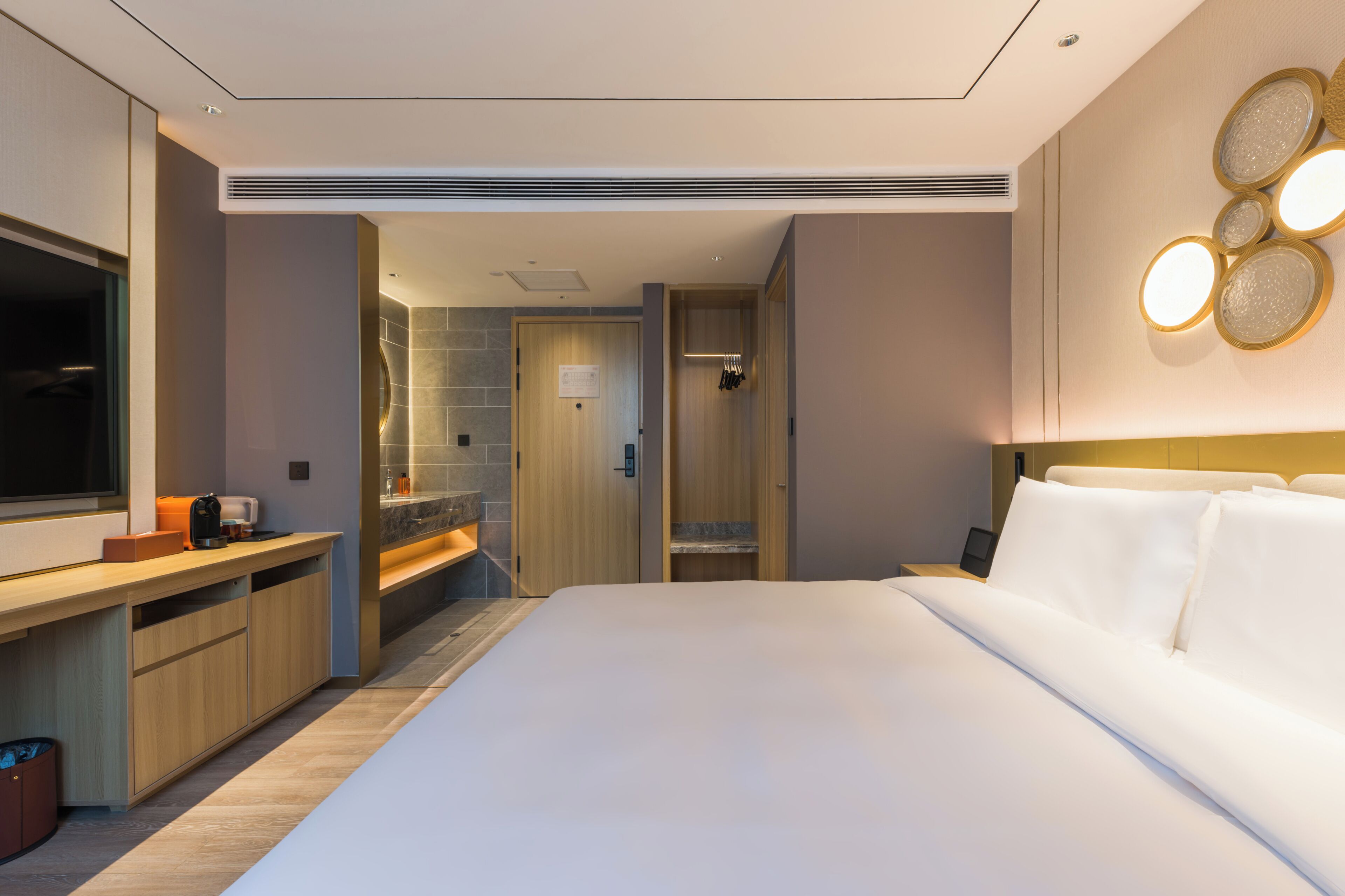 A modern hotel room with a large bed, a vanity with a mirror, a shower area, and a small seating area with a table.