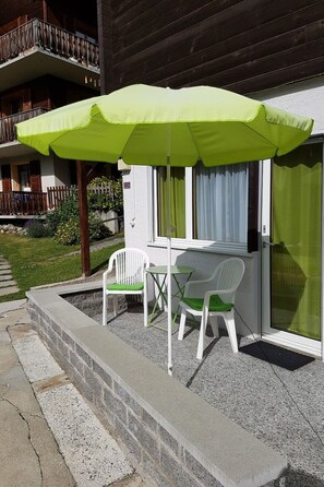A patio with a green umbrella, two white chairs, and a small table. - Ferienwohnungen Silberblick, (Grächen), by Interhome (Grächen)