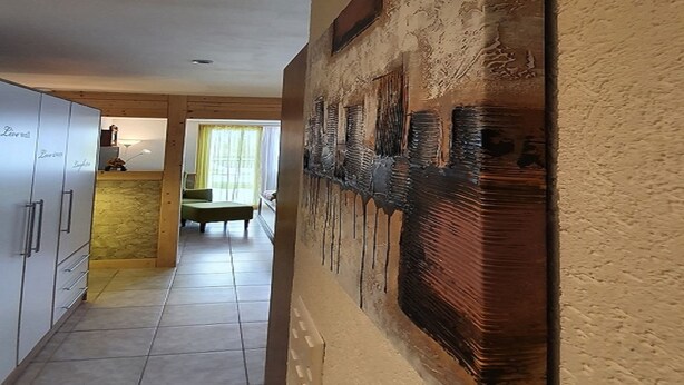 Een gang met een eetgedeelte, een keuken en een groot abstract schilderij aan de muur.
