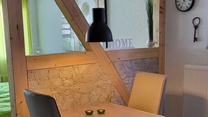 Een eetgedeelte met een houten tafel, twee stoelen, een hanglamp, een stenen muur en een raam met uitzicht op groen.