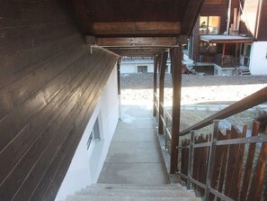 Una escalera de madera conduce a un espacio al aire libre cubierto con vista a un edificio al fondo.