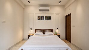 A hotel room with a large bed, two bedside tables, a wooden headboard, an air conditioning unit, and a door. - Unwild India Pilibhit Tiger Reserve (Puranpur)