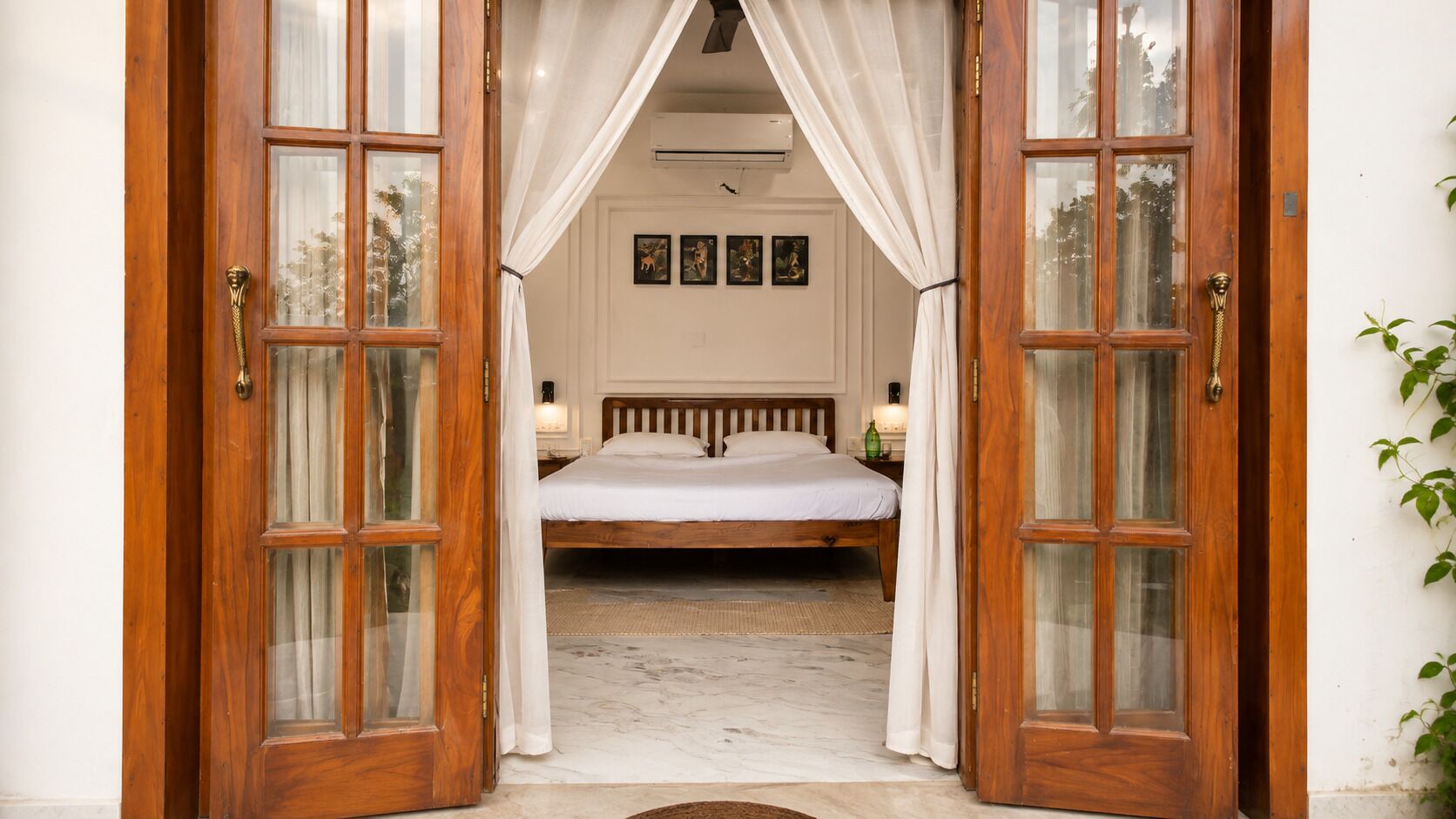 A bedroom with a wooden bed, white curtains, and a view of the outside.