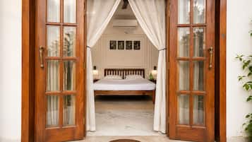 A bedroom with a wooden bed, white curtains, and a view of the outside.