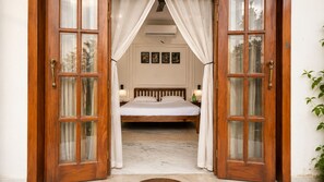 A bedroom with a wooden bed, white curtains, and a view of the outside.