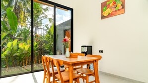 A dining area with a table and chairs, a coffee machine, and a view of a garden through a glass door. - Bugenvil Villa Ubud (Kabupaten Gianyar)