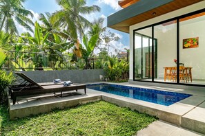 A modern outdoor pool area with a glass-enclosed patio, a lounge chair, and a dining table. - Bugenvil Villa Ubud (Kabupaten Gianyar)