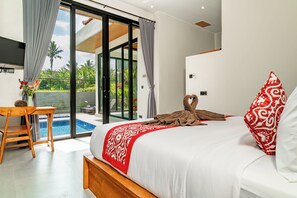 A modern hotel room with a large bed, a small table, a chair, and a view of a swimming pool. - Bugenvil Villa Ubud (Kabupaten Gianyar)