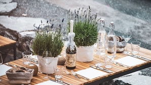 Une table à manger d’extérieur, agrémentée de verres à vin, de bouteilles et d’une plante en pot.