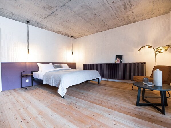 A bedroom with a bed, bedside tables, a radiator, a chair, a table with a vase, and a wall-mounted picture.