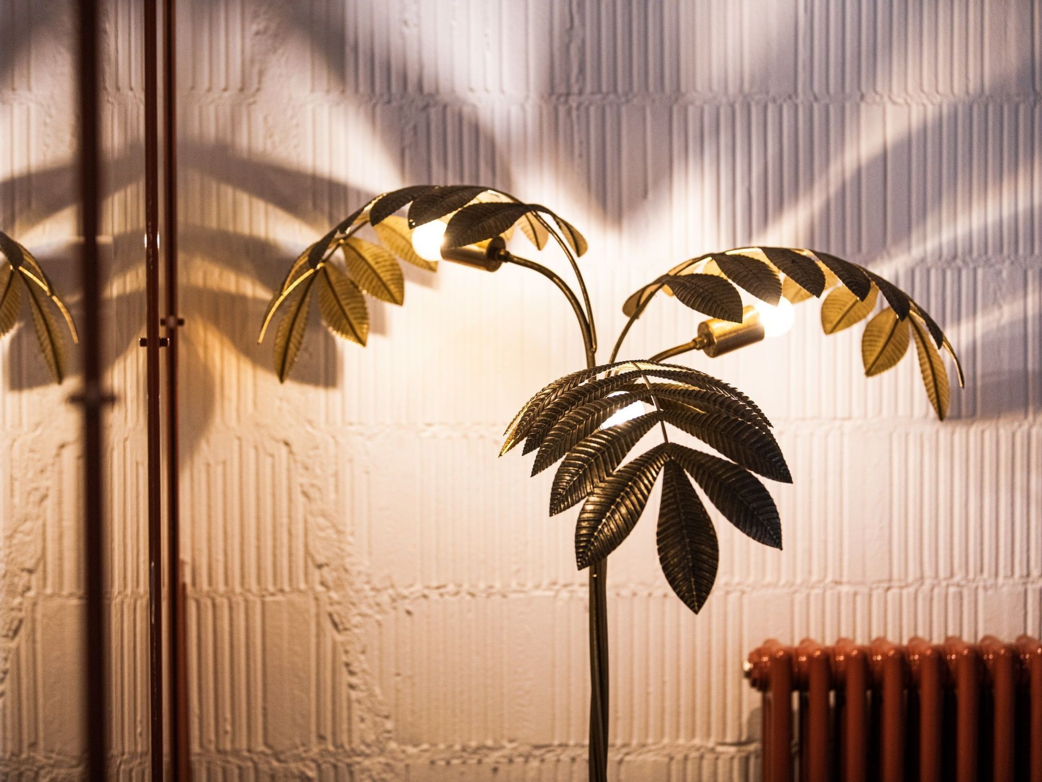 Eine Stehlampe mit blattformartigem Design vor einer strukturierten Wand.