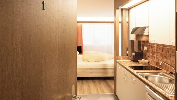 A hotel room with a kitchenette, a bed with a white pillow, and a door marked with the number 1. - Casa Viva, (Bad Ragaz), by Interhome (Bad Ragaz)