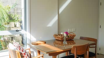 Un coin repas avec une table en verre, des chaises en bois, un panier en osier et un vase rempli de fleurs.