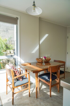 A dining area with a glass table, wooden chairs, a wicker basket, and a vase with flowers.