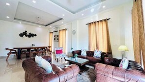 A living room with a sofa set, a coffee table, a dining table with chairs, and a wall clock. - Nik Banquet Hall Chhatarpur Delhi (New Delhi)