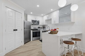 A modern kitchen with white cabinetry, stainless steel appliances, a central island with stools, and pendant lighting. - 2BR Villa w/ Bonus Lounge & Wine Fridge, Indoor & Outdoor Pools, Near Coligny (Hilton Head Island)