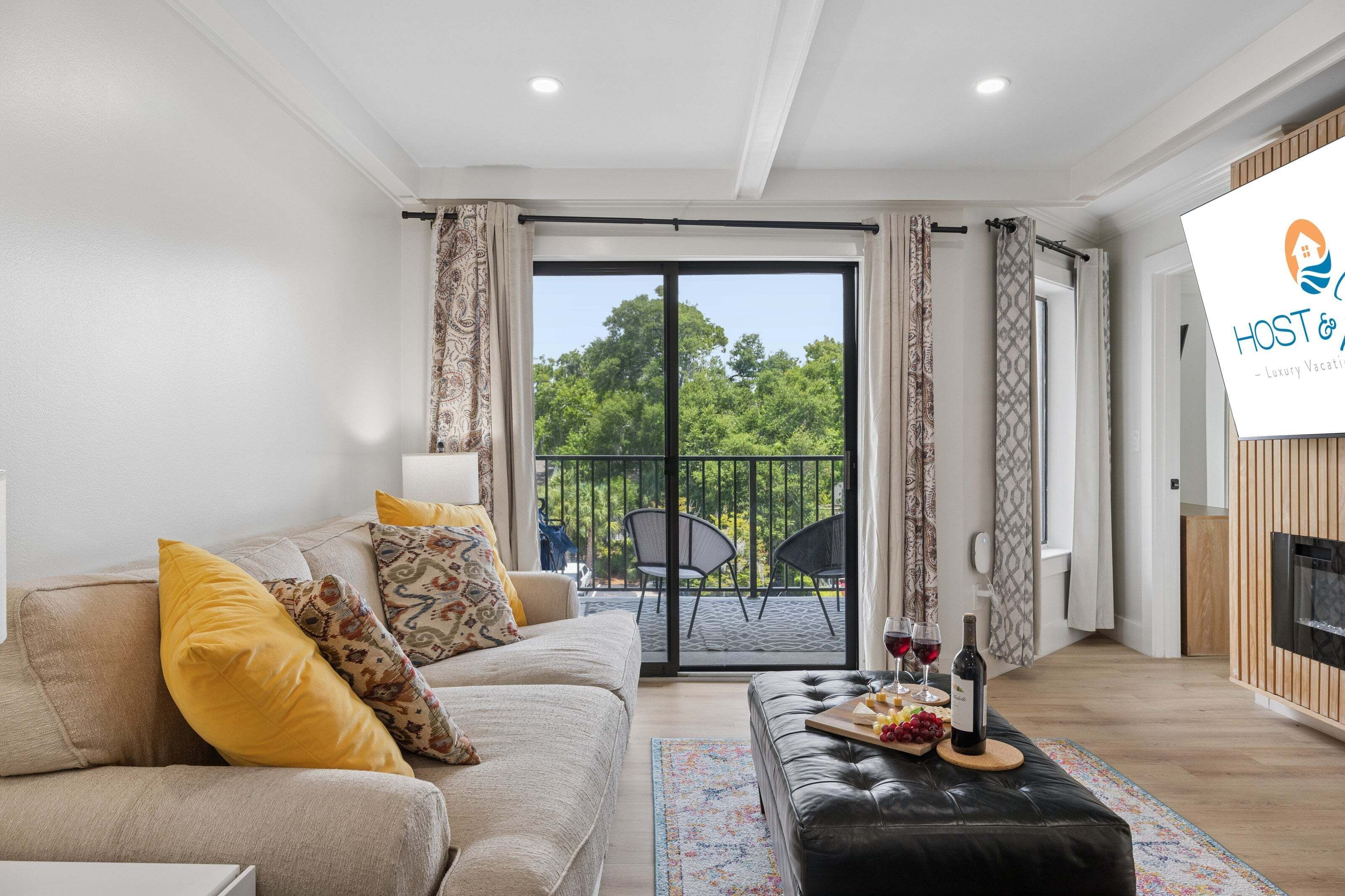 A modern living room with a sofa, ottoman, and a dining table set with wine glasses and fruit.