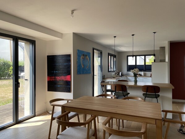A modern kitchen with a dining area, large windows, and artwork on the walls. - A 5-minute walk to the beach, quiet house, ideal for families (Saint-Lunaire)