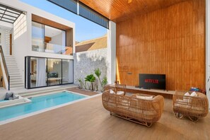 Ein moderner Außenbereich mit Pool, Korbmöbeln, einem Fernseher und einer Steinwand.