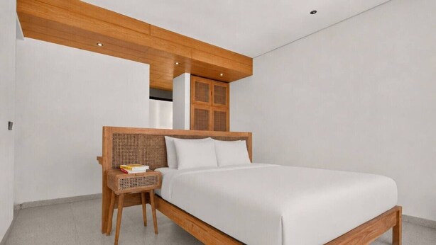 A modern bedroom with a wooden bed frame, a nightstand, and a woven chair. - Casa Cemagi - Luxury 3BR Villa Near Beach by Orivista (Kecamatan Mengwi)