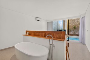 A modern bathroom with a freestanding bathtub, a wooden vanity, and a view of a pool and outdoor seating area. - Casa Cemagi - Luxury 3BR Villa Near Beach by Orivista (Kecamatan Mengwi)