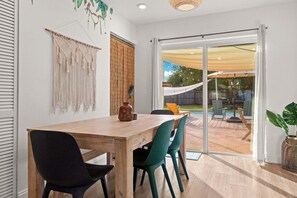 A dining area with a wooden table and chairs, a macrame wall hanging, and a sliding glass door leading to an outdoor patio. - Family-Friendly Seminole Pool Retreat | Fire Pit (Seminole)