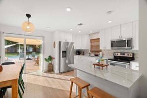 A modern kitchen with white cabinets, stainless steel appliances, and a large island. - 3BR Seminole Pool Home | Private Pool & Fire Pit (Seminole)