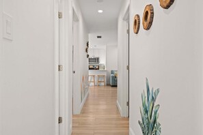 A hallway with white walls, wooden flooring, and a kitchen area in the distance. - Family-Friendly Seminole Pool Retreat | Fire Pit (Seminole)