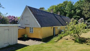 Un bâtiment jaune avec un toit sombre, une petite fenêtre et une porte.