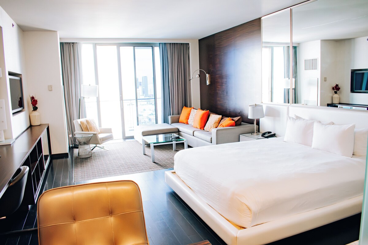 Quarto de hotel com uma cama grande, um sofá, uma escrivaninha, uma cadeira e uma televisão.