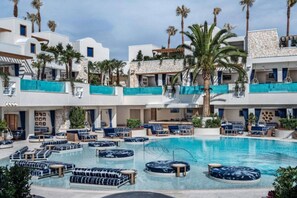A pool area with lounge chairs and a circular seating area, surrounded by multi-story buildings with balconies and palm trees.