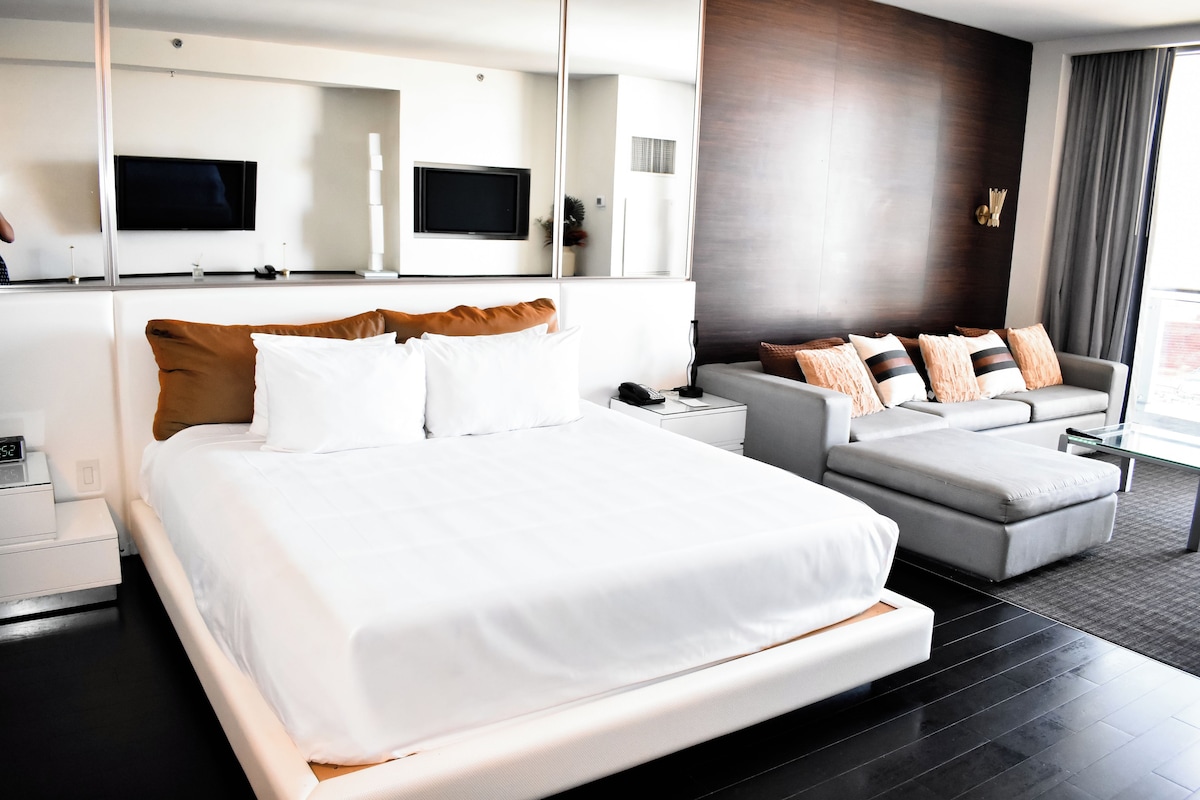 Quarto de hotel moderno com uma cama grande, um sofá, uma escrivaninha e uma televisão de tela plana.