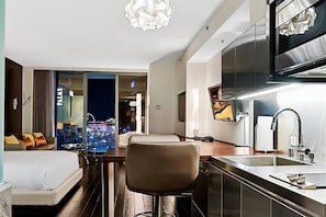 Habitación de hotel con cama, escritorio, silla, zona de cocina y vistas a la ciudad.