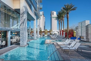 A hotel pool area with multiple pools, lounge chairs, and palm trees.