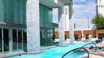A swimming pool area with clear blue water, surrounded by glass walls and columns with mosaic tile patterns.