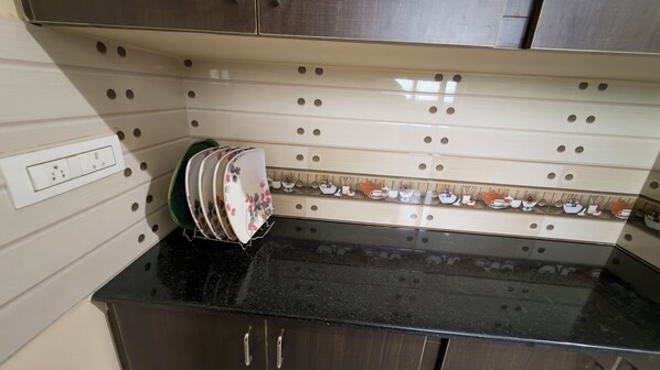 A kitchen with a black countertop, a dish rack with plates, and a backsplash with a pattern of holes.