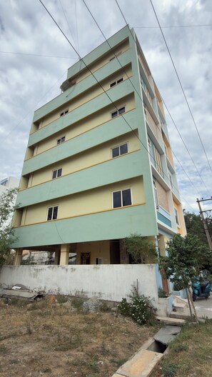 A multi-story building with a flat roof, multiple windows, and a concrete base. - Govinda Nivas Homestay (Tirupati)