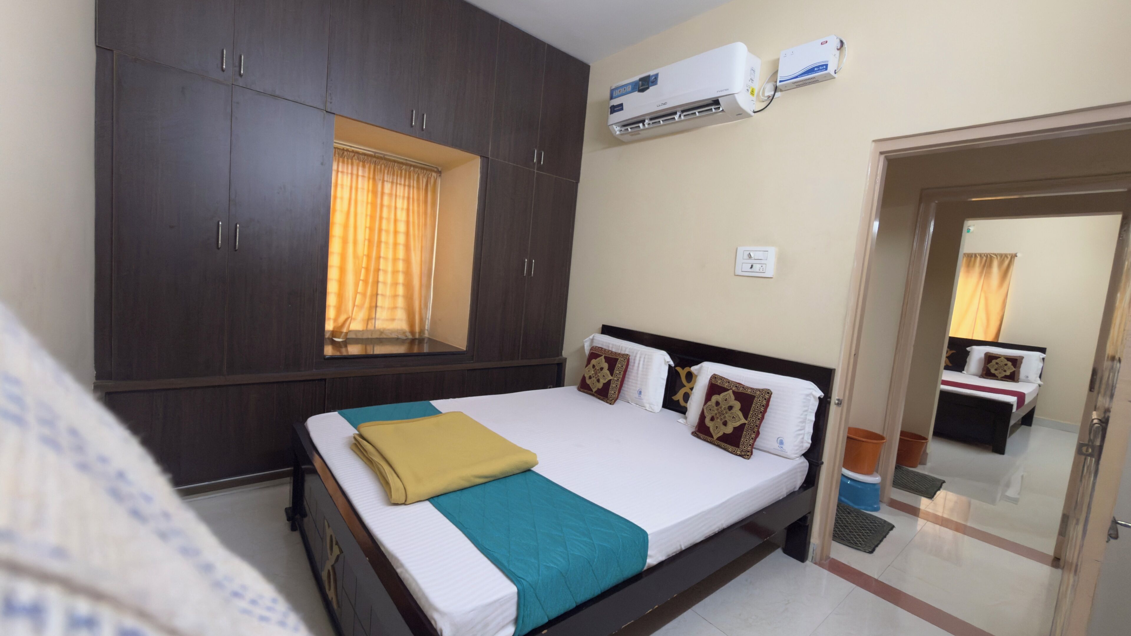 A hotel room with a bed, wardrobe, air conditioning unit, and a window with curtains.
