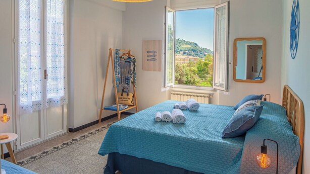 Una camera da letto con un letto, una finestra vista, una sedia a dondolo e uno specchio fissato alla parete.