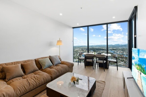 Una sala moderna con sofá, mesa de centro, lámpara, mesa de comedor, sillas y un ventanal con vista a la ciudad.