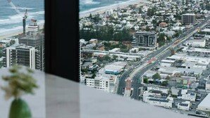 Blick aus einem Fenster auf eine Küstenstadt mit Gebäuden, Straßen und dem Meer.