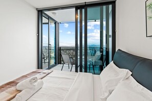 Un dormitorio con cama, vistas a un balcón con una silla y un paisaje urbano.