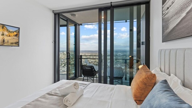 Un dormitorio con una cama grande, vistas a una ciudad a través de un ventanal corredero y un cuadro en la pared.