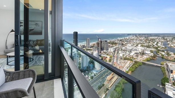 Un balcon avec une porte vitrée, un fauteuil en osier et une vue sur un paysage urbain avec des bâtiments et une rivière.
