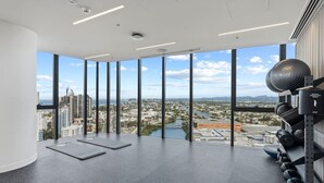 Une salle de sport située dans un immeuble de grande hauteur, dotée de grandes fenêtres, de tapis de sol et d’un support à poids fixé au mur.