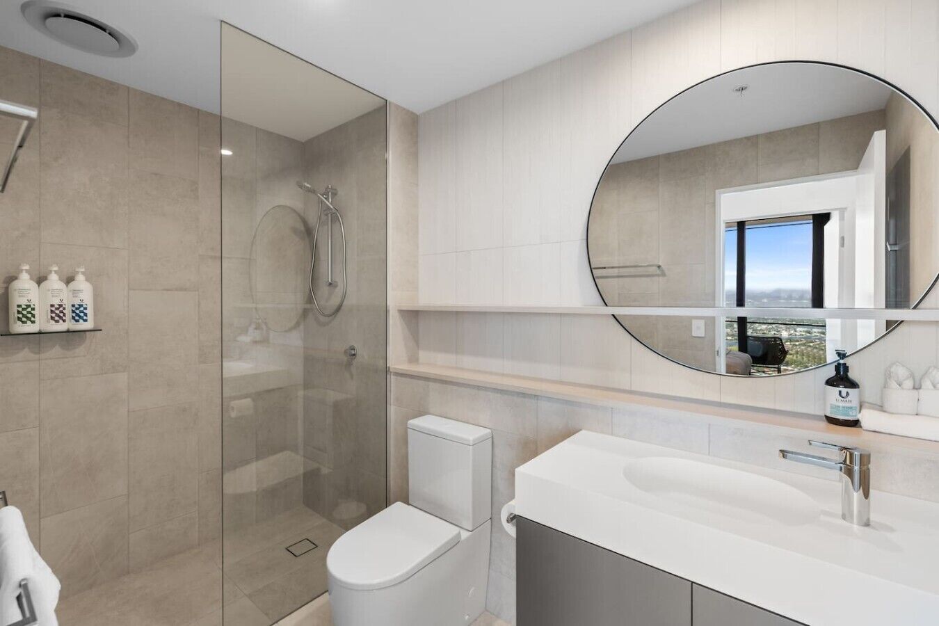 A modern bathroom with a glass-enclosed shower, a toilet, and a vanity with a large mirror.