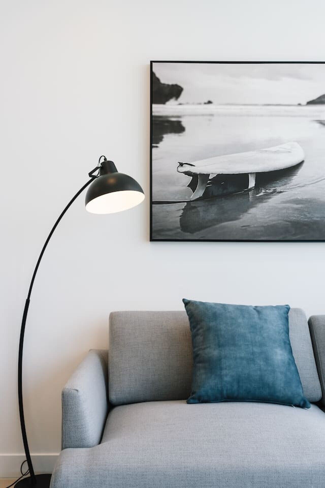 A grey sofa with a blue pillow and a black floor lamp.