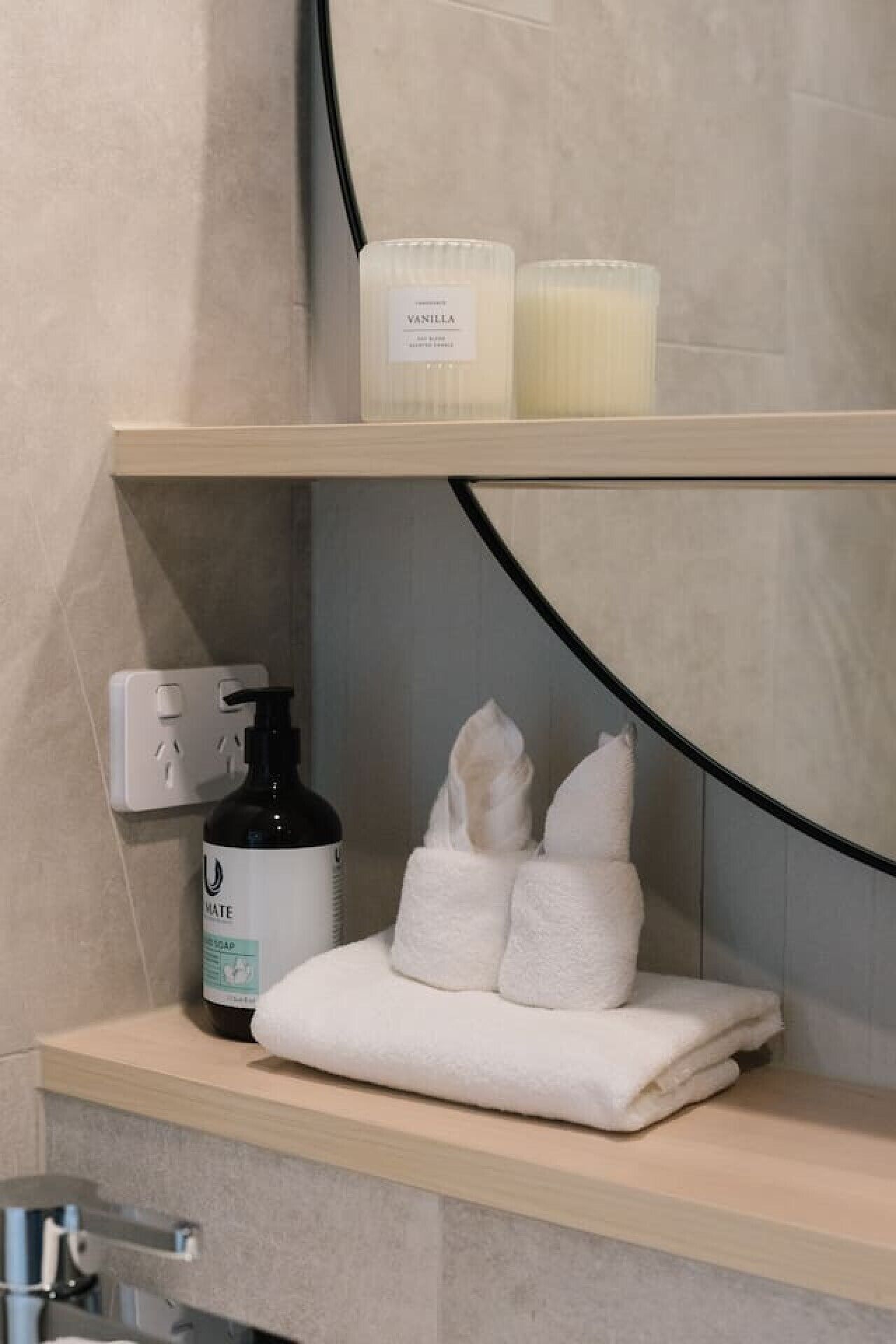 A bathroom shelf with a bottle of soap, a towel, and two candles.